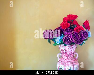 Bellissimi fiori rossi, viola e blu in vaso di ceramica vintage su sfondo giallo con spazio per la copia. Foto Stock