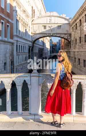 Giovane donna con gonna rossa, turistica su un ponte sul Rio di Palazzo, dietro Ponte dei Sospiri, Venezia, Veneto, Italia Foto Stock