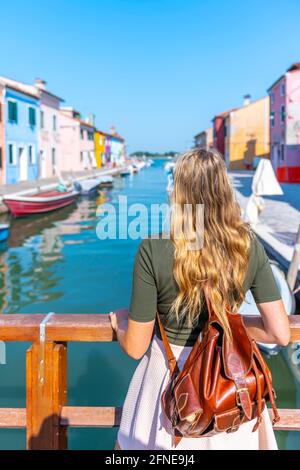 Giovane donna di fronte a case colorate, canale con barche e facciate colorate casa, Burano Island, Venezia, Veneto, Italia Foto Stock