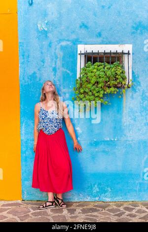 Giovane donna di fronte alla casa blu, facciate colorate, Isola di Burano, Venezia, Veneto, Italia Foto Stock