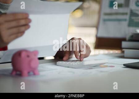 Donna calcolando il suo debito. Mano di donna calcolando le sue spese mensili durante la stagione fiscale con monete, calcolatrice e banca di conto. Foto Stock