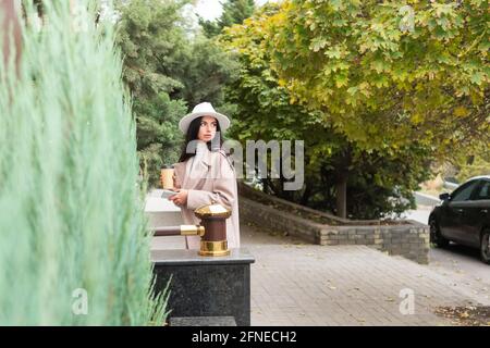 donna con un telefono e una tazza di caffè passeggiate lungo il marciapiede e guarda indietro Foto Stock