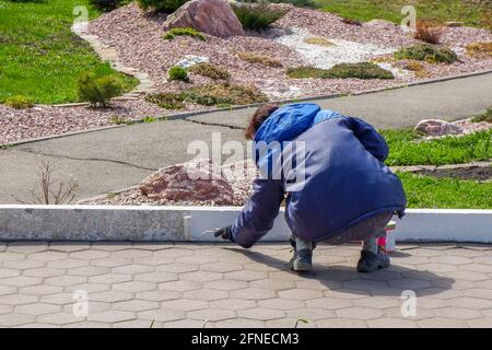 un dipendente dipinge il cordolo con vernice bianca. servizi urbani, primo piano Foto Stock