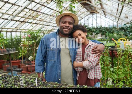 Ritratto di felice padre abbracciando suo figlio e sorridono alla macchina fotografica mentre si è in piedi in serra Foto Stock