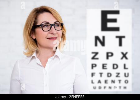 ritratto della donna matura di affari allegra pensierosa negli occhiali con grafico di prova degli occhi su sfondo bianco Foto Stock