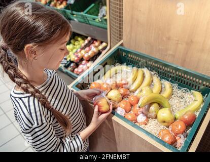 Una bambina sceglie le mele e le banane confezionate singolarmente nel negozio. Foto Stock