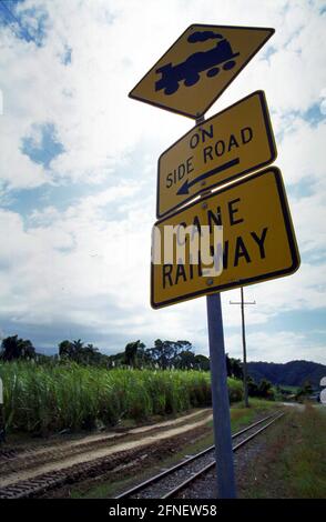 Tracce e segnali stradali della Cané Railway vicino a Cairns. Sullo sfondo una piantagione di canna da zucchero. [traduzione automatizzata] Foto Stock