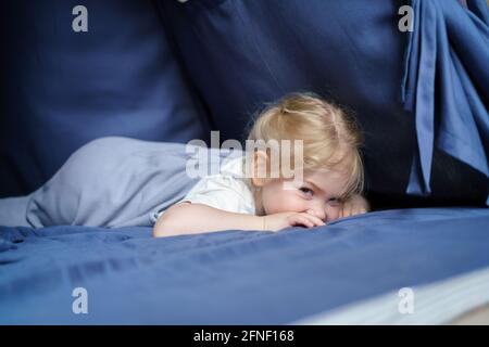 Bambina dolce con i capelli biondi che si trovano all'interno dei bambini giocare tenda o tipi e guardare giocosamente alla macchina fotografica mentre godendo il tempo libero nella stanza dei bambini a casa o asilo. Concetto di infanzia felice Foto Stock