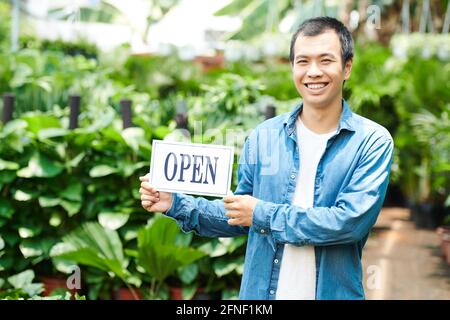 Ritratto di giovane sorridente che apre vivaio pianta e invitante clienti Foto Stock