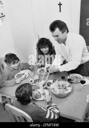 I genitori sono seduti al tavolo da pranzo con i loro due bambini che mangiano spaghetti e insalata. [traduzione automatizzata] Foto Stock