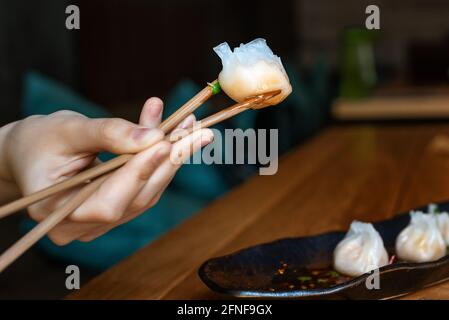 Chiudi la mano femminile con gnocchi cinesi caldi. Dim sum cinese al vapore con chopsticks. Gnocchi asiatici su un piatto in un ristorante. Foto Stock