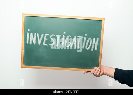 Mano che tiene una lavagna con la parola INVESTIGAZIONE scritto a mano gesso Foto Stock