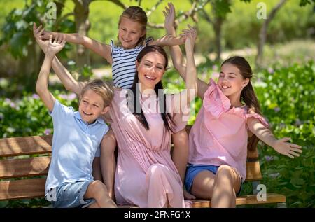 Madre felice e i suoi tre bambini preziosi seduti sul banco del Parco. Grande famiglia avendo tempo e scherzando nel parco della città il giorno d'estate. Concetto di amore. Foto Stock