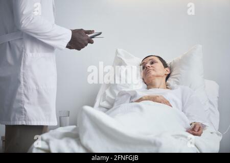 Donna matura sdraiata a letto e che parla con il medico a. ospedale Foto Stock