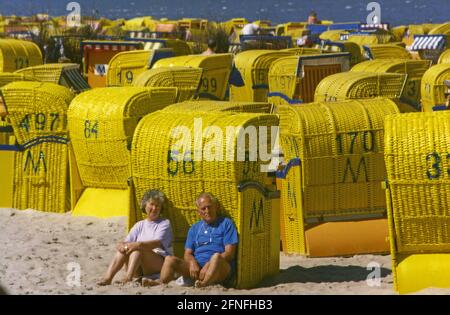 Una coppia siede sulla spiaggia del Mare del Nord davanti alle sedie a sdraio. [traduzione automatizzata] Foto Stock