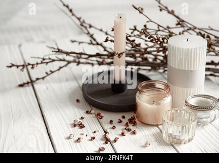 Composizione accogliente con candele decorative e rami di alberi giovani su una superficie di legno in stile rustico. Foto Stock