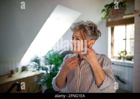 Donna anziana in bagno pettinando i capelli a casa, stile di vita ecologico e sostenibile. Foto Stock