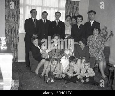 anni '60, storica, dopo un battesimo, una grande famiglia, di diverse generazioni, Tutti si riuniscono in una stanza anteriore per un gruppo di foto di famiglia, tra cui uomini, donne, bambini e bambini, Inghilterra, Regno Unito. Foto Stock