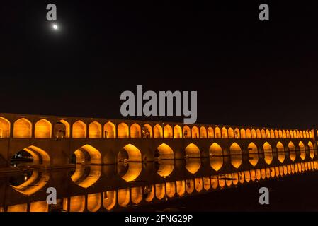 Luna piena sopra il ponte illuminato Siosepol, uno dei ponti storici sul fiume Zayanderud a Isfahan, Iran. Foto Stock