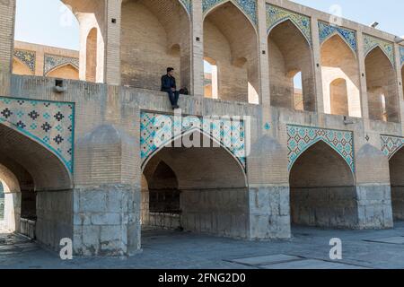 Uomo rilassante sullo storico ponte Khaju sul fiume Zayanderud a Isfahan, Iran Foto Stock