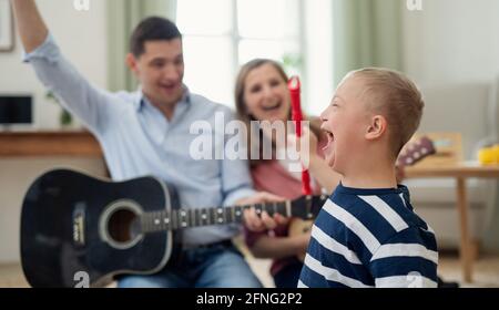 Allegro ragazzo sindrome giù con i genitori che suonano strumenti musicali, ridendo. Foto Stock