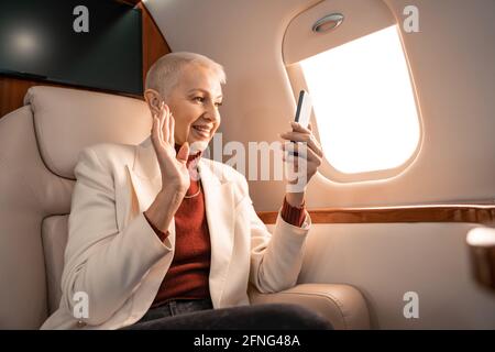 Donna d'affari sorridente che sventolava la mano durante la videochiamata con smartphone in piano Foto Stock