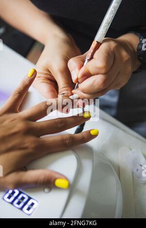 Dall'alto di raccolto manicurista irriconoscibile facendo arte del chiodo per cliente femminile in salone di bellezza alla luce del giorno Foto Stock
