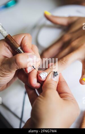 Dall'alto di raccolto manicurista irriconoscibile facendo arte del chiodo per cliente femminile in salone di bellezza alla luce del giorno Foto Stock