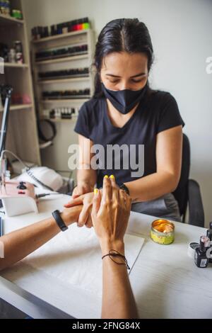 manicurista massaggiare le mani del cliente senza volto dopo l'applicazione di olio cosmetico in studio unghie Foto Stock