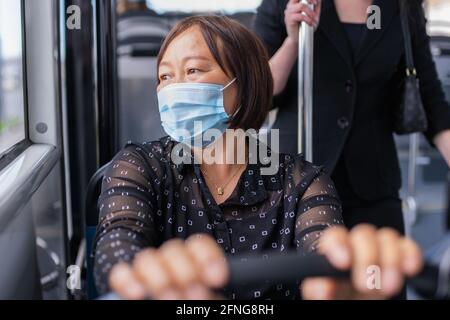 Donna asiatica seduta su un autobus che guarda all'esterno: Fuoco selettivo. Sicurezza e vacanze dopo il concetto di blocco. Foto Stock
