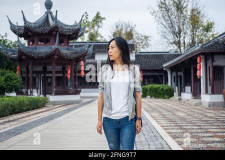 Bella donna asiatica che cammina in un giardino cinese con architettura tradizionale sullo sfondo Foto Stock