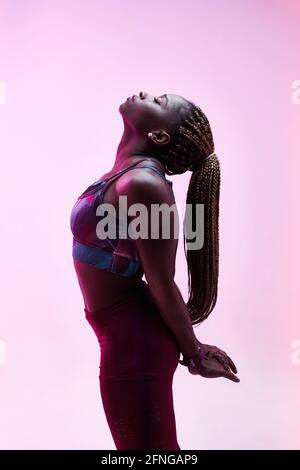 Vista laterale dell'atleta etnica femminile con trecce afro e. mani aggrappate dietro la schiena con occhi chiusi Foto Stock