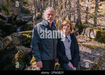 Deliziati esploratori seduti vicino albero in foresta e di riposo durante trekking mentre si guarda la macchina fotografica Foto Stock