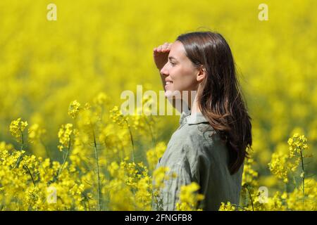 Donna felice che protegge dal sole con la mano in un campo fiorito giallo Foto Stock