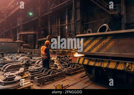 Lavoratrice di fonderia in officina con prodotti metallici finiti fusi fonditi fonditi presso la fabbrica di acciaierie. Foto Stock