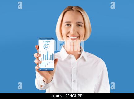 Donna allegra che mostra smartphone con grafici e diagrammi sullo schermo Foto Stock