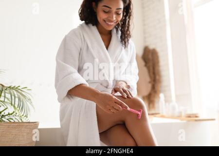 Gambe di rasatura Black Female in bagno, fuoco selettivo su Razor Foto Stock