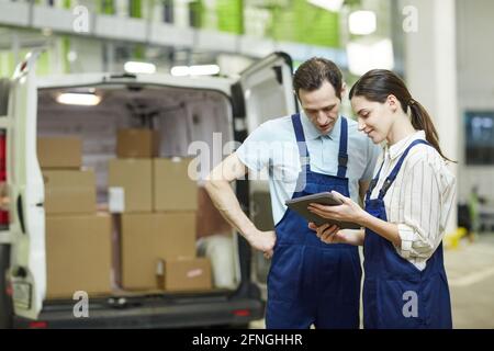 Due colleghi che utilizzano un tablet pc mentre si trovano in prossimità del camion lavorano in magazzino Foto Stock