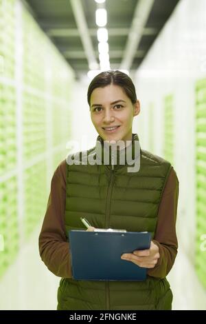 Ritratto di giovane donna con documento sorridente alla fotocamera mentre in piedi in magazzino Foto Stock