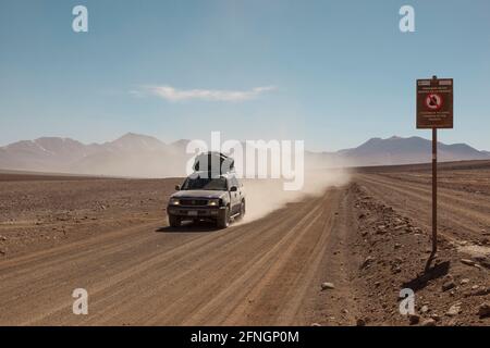 Sullo sfondo di vulcani, un veicolo fuoristrada 4x4 attraversa il paesaggio desertico della Bolivia in un safari turistico terrestre. Foto Stock