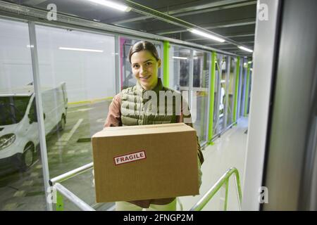 Ritratto di giovane donna che tiene scatola di cartone e sorridente a. macchina fotografica che ha ottenuto il suo pacco Foto Stock