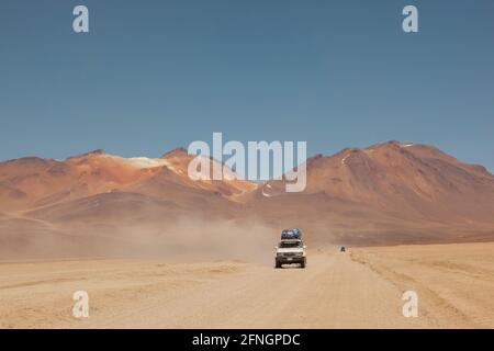 Sullo sfondo di vulcani, un veicolo fuoristrada 4x4 attraversa il paesaggio desertico della Bolivia in un safari turistico terrestre. Foto Stock