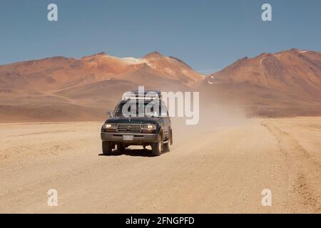 Sullo sfondo di vulcani, un veicolo fuoristrada 4x4 attraversa il paesaggio desertico della Bolivia in un safari turistico terrestre. Foto Stock