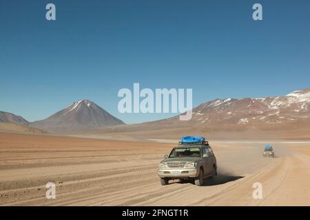 Sullo sfondo di vulcani, un veicolo fuoristrada 4x4 attraversa il paesaggio desertico della Bolivia in un safari turistico terrestre. Foto Stock