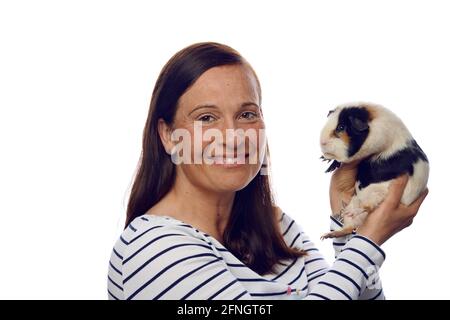 Donna amorevole felice che tiene in su il suo porcellino di cavia dell'animale domestico dentro le mani girandosi per guardare la fotocamera con un sorriso amichevole isolato su bianco Foto Stock