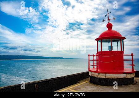 Faro rosso che si affaccia sul mare blu e cielo a Nazaré, Portogallo Foto Stock