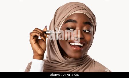 Donna nera musulmana che applica moisturizer o acido ialuronico sulla faccia Foto Stock