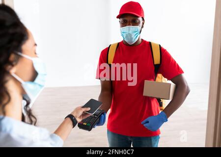 Uomo nero che tiene il cliente della macchina del POS che paga con lo smartphone Foto Stock