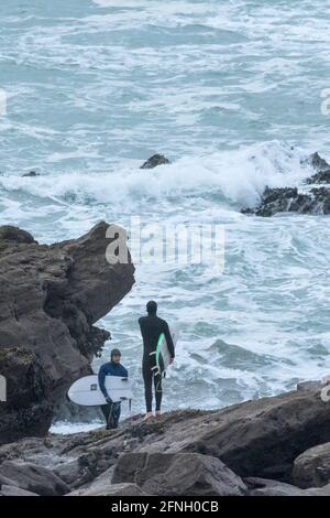 Surfisti che trasportano le loro tavole da surf e si levano in piedi su rocce alla ricerca di un'area di lancio sicura in mare mosso a Little Fistral a Newquay in Cornovaglia. Foto Stock