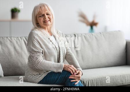 Donna anziana che soffre di dolore alle gambe a casa Foto Stock